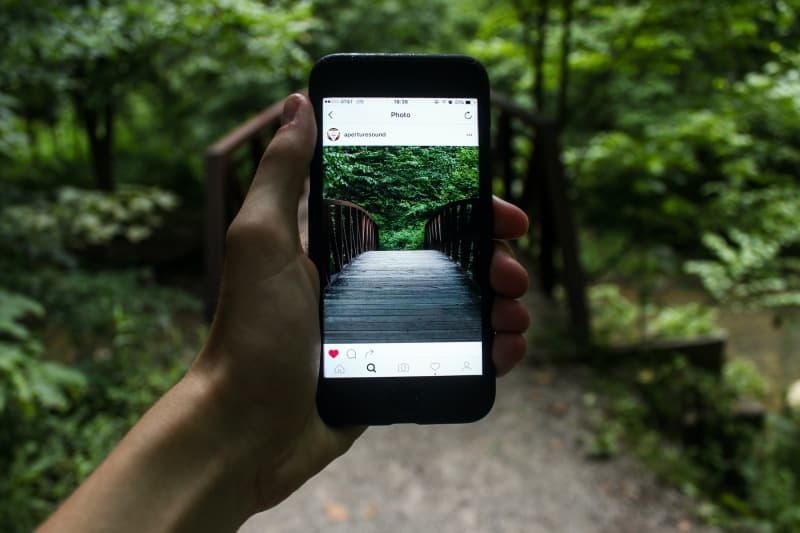 Person hält Smartphone, das tagsüber eine Brücke fotografiert